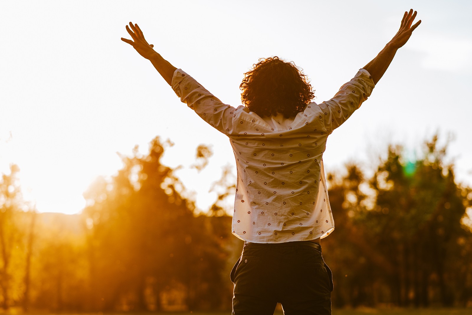 A man stands with his arms above his head while taking in the setting sun. An online therapist in Oregon can offer support in cultivating gratitude and more. Search “Oregon online therapist” today to learn more. 