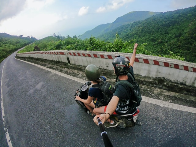 two people riding scooter on road near foresty cliff exhilerated