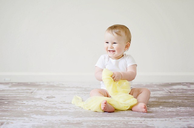 Smiling baby sitting on the floor with a yellow blanket. Discover joy blog post from online therapist in Oregon for anxiety treatment and codependency counseling in Tigard, OR.