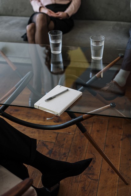 online therapy in Oregon | counseling in Tigard, OR | therapy in Tigard, OR | online therapist in Oregon | Discover Counseling A journal and pen on a glass table with three different people's feet are shown below the table. The could represent a couple seeking relationship counseling at Discover Counseling. Further, the couple could be discussing depression treatment in Tigard, Oregon, or if they should try online counseling in Oregon with Discover Counseling's therapists.