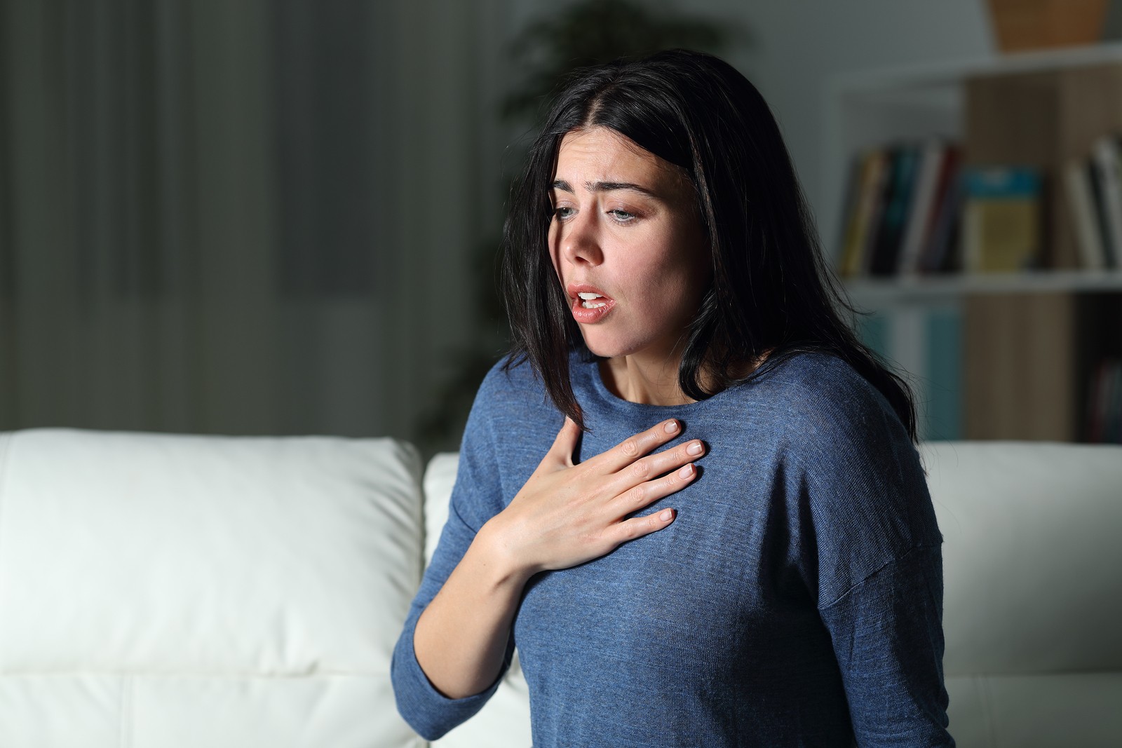 Woman suffering an anxiety attack alone in the night on a couch at home due to post-COVID social anxiety in Tigard, OR. You can get anxiety treatment with online therapy in Oregon here.