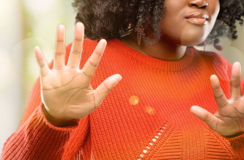 Image of a woman in an orange sweater with her hands up showing how hard change can be without life transition counseling. Those feelings of avoidance cna get easier after working with an online therapist of therapy for life transitions.