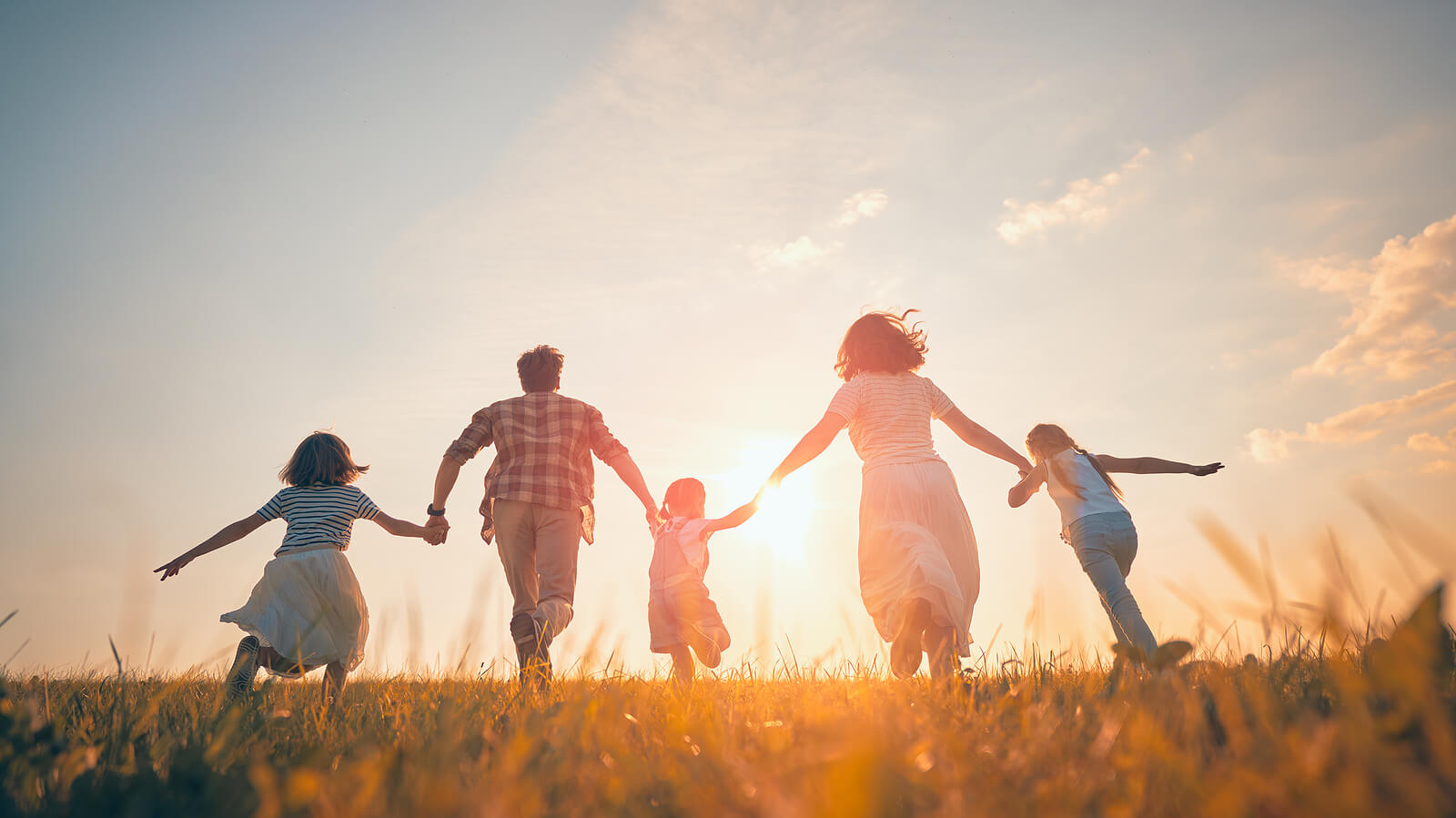 Family of four holding hands and running together in a field representing the healthy relationships that come with setting boundaries. Learn how to set your own boundaries with online therapy in Oregon.
