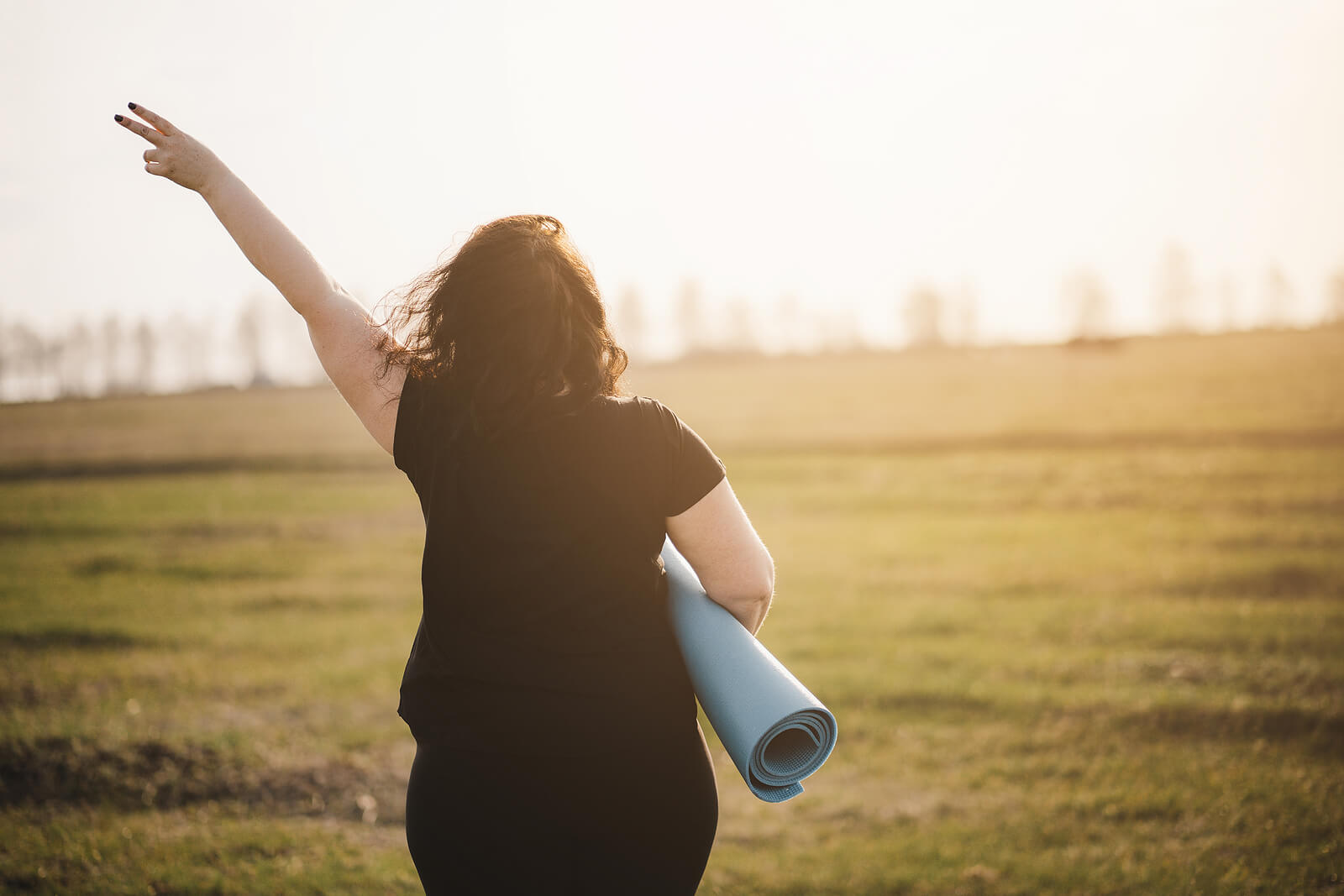 A woman holds up her hands in a peace sign while walking with a yoga mat across a field. Anxiety counseling in Tigard, OR can offer support in overcoming personal struggles. Learn more about therapy for anxiety Tigard, OR today.
