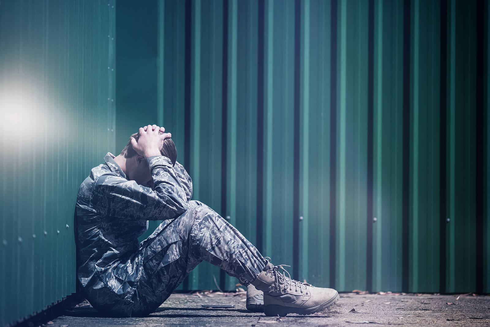A man in military fatigues sits against a wall with hands over the back of his neck. This could symbolize the struggles of anxiety that anxiety counseling in Tigard, OR can help you address. Learn how an online therapist in Oregon can offer support with coping with social anxiety in Oregon and other services. 
