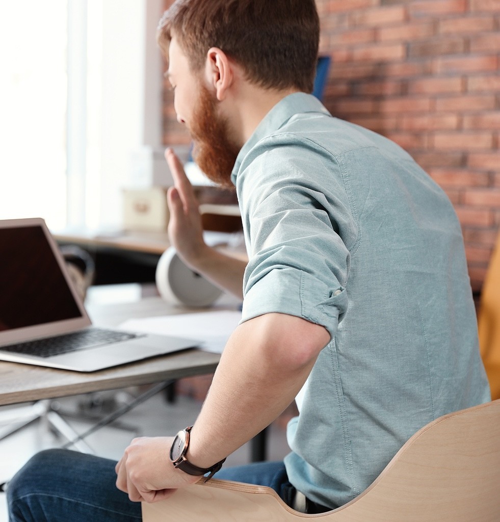 A man waves at a laptop screen while sitting at a desk. This could represent the convenience of online therapy in Oregon that an online therapist in Oregon can offer. Search for an Oregon online therapist for more support. 
