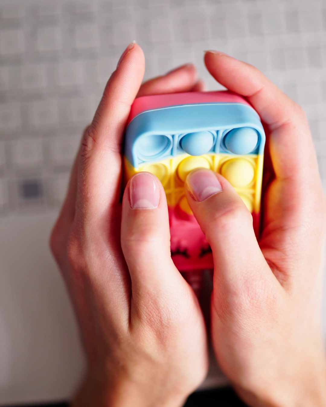 Hands holding a colorful pop-it toy, pressing the bubbles for stress relief. Anxiety treatment in Tigard, OR can help with high-functioning anxiety and more.