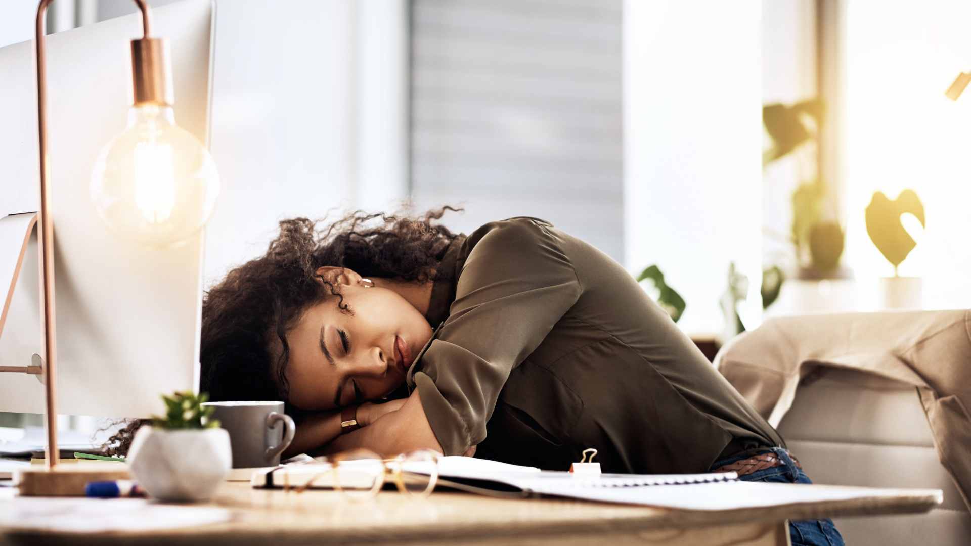 A person with curly hair sleeps at a desk in an office setting, resting their head on a notebook. Perfectionism in women in Tigard, OR can be helped with therapy.