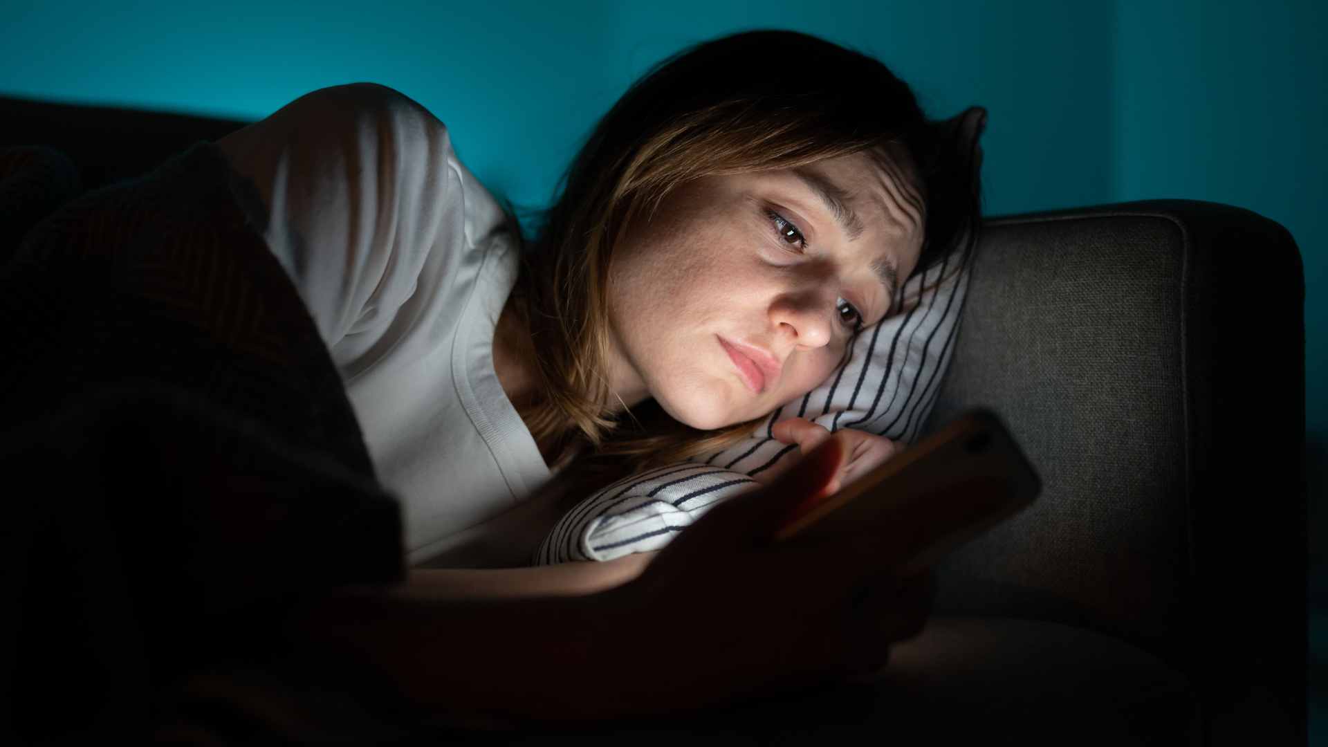 Person lying on a couch in dim light, looking at a smartphone with a concerned expression. Anxiety treatment in Tigard, OR can help with high-functioning anxiety and more.