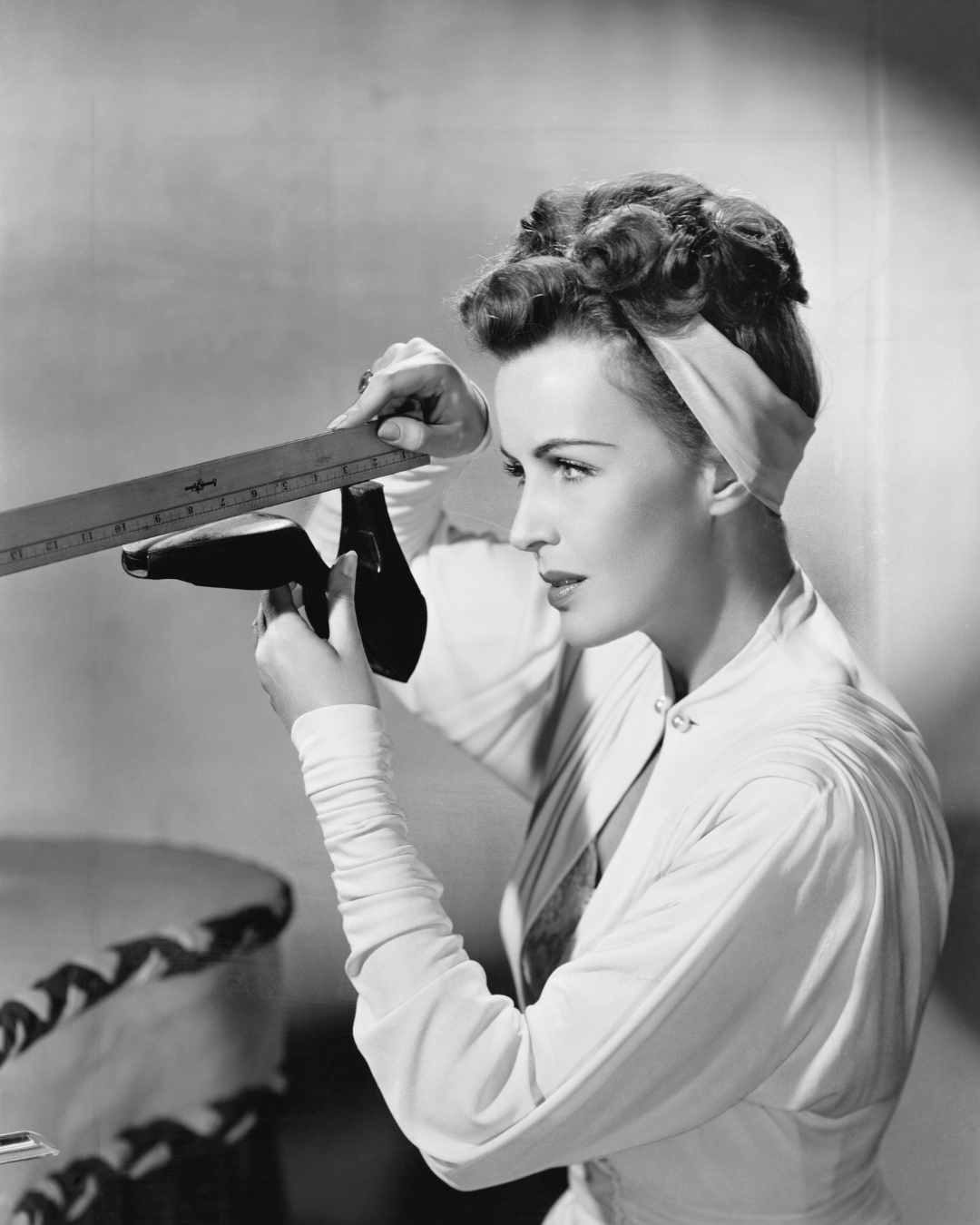 Woman measuring a shoe with a ruler, wearing a headband and a light-colored blouse, in a vintage-style black and white photograph. Perfectionism in women in Tigard, OR can be helped with therapy.