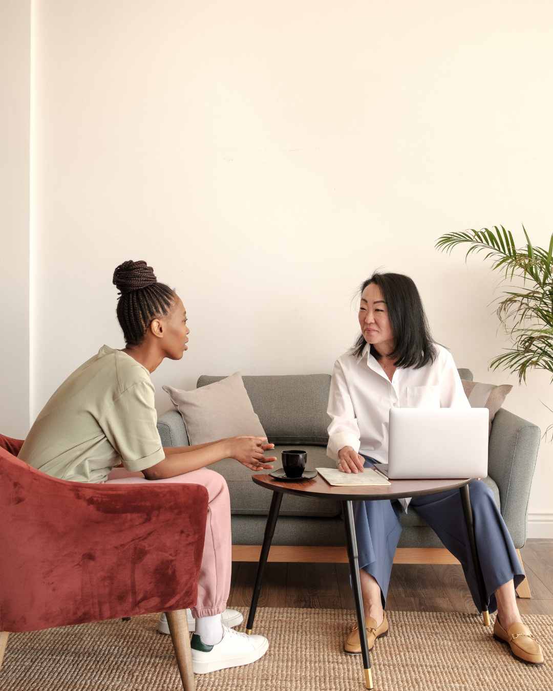 Two people sitting on a sofa and chair, engaged in conversation. A laptop and notebook are on a small table between them. Anxiety treatment in Tigard, OR can help with high-functioning anxiety and more.