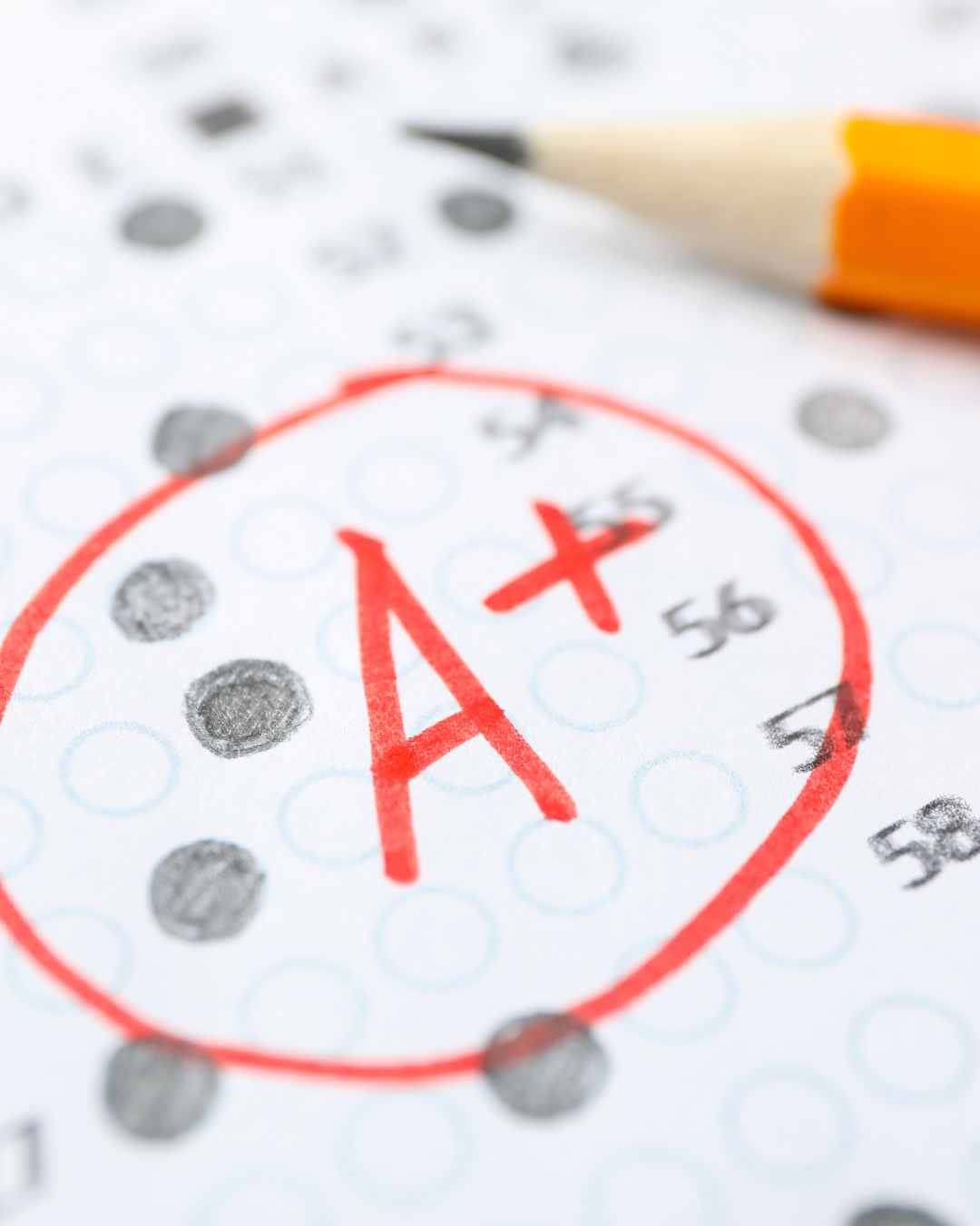 A close-up of a multiple-choice answer sheet with a red A+ circled and a sharpened yellow pencil placed on top.