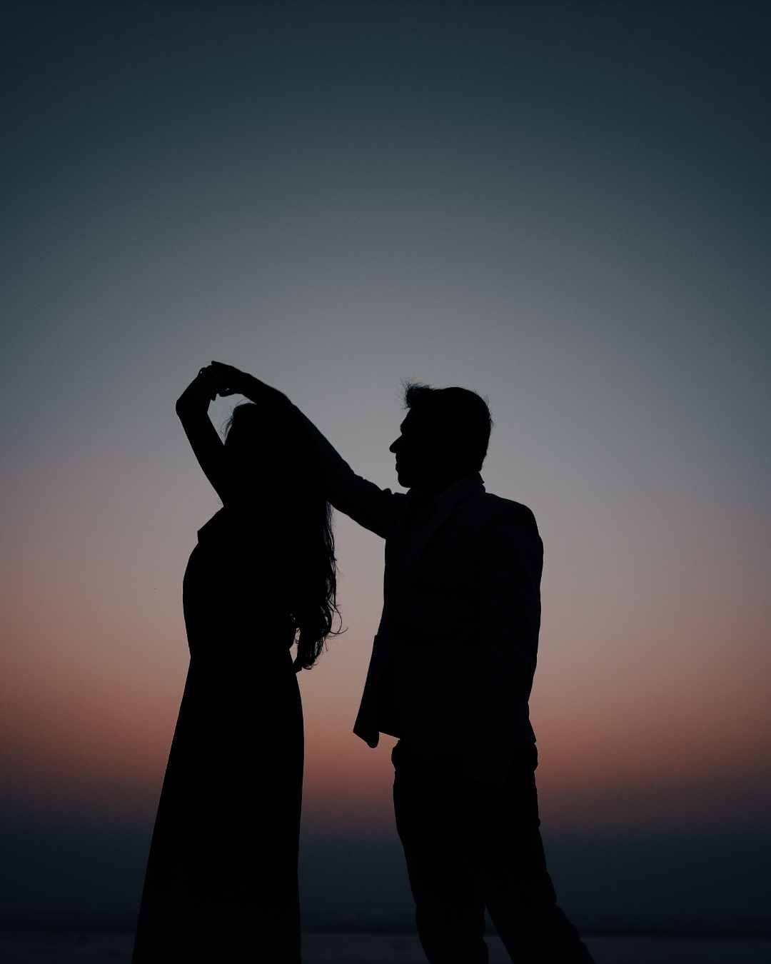 Silhouette of a couple dancing at sunset, with a gradient sky transitioning from blue to orange in the background.