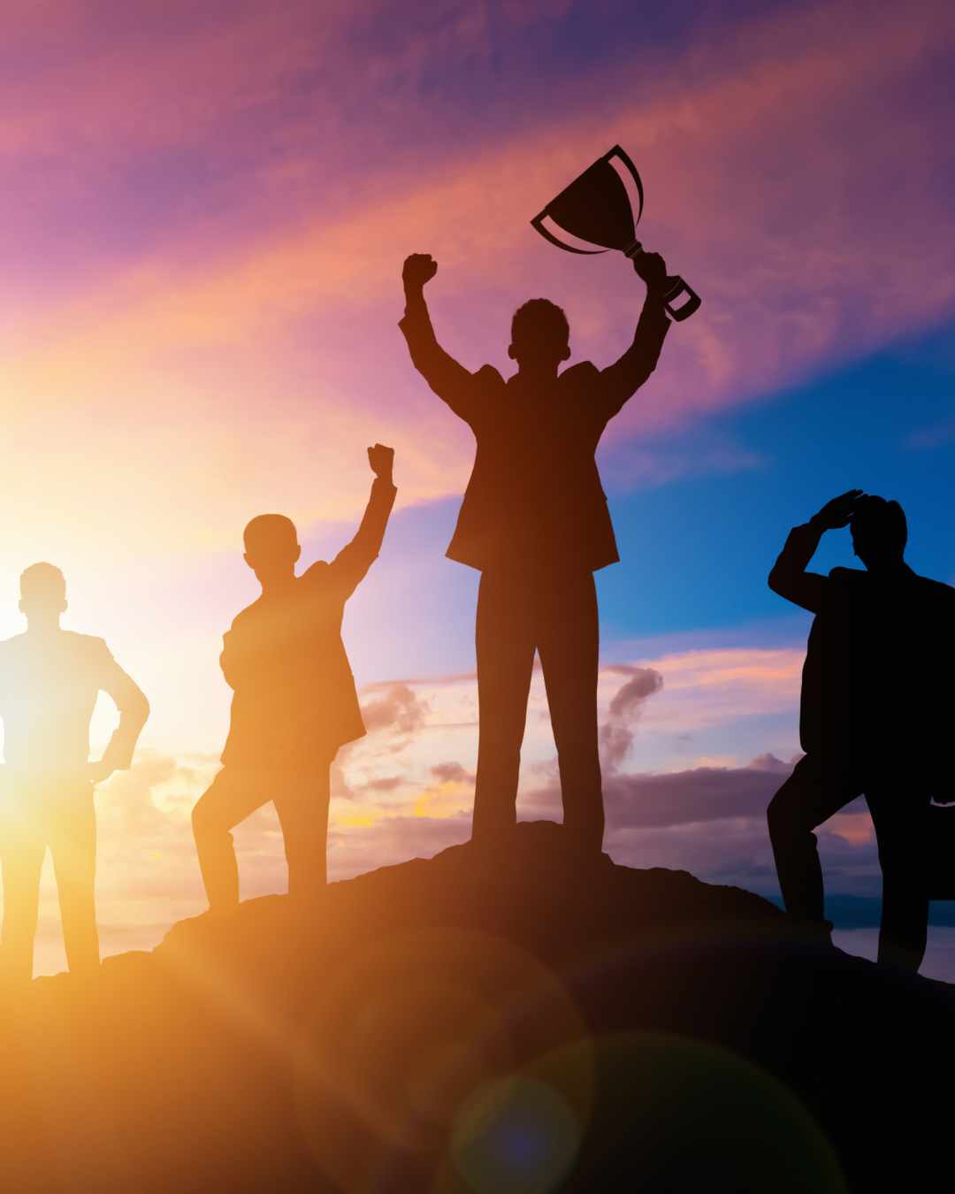 Perfectionism Rewarded | High Achiever Therapy in Tigard, OR | Perfectionism Counseling Online in Oregon Silhouettes of four people on a hill at sunset, with one holding a trophy and raising their arm in victory while others stand nearby. Perfectionism rewarded.