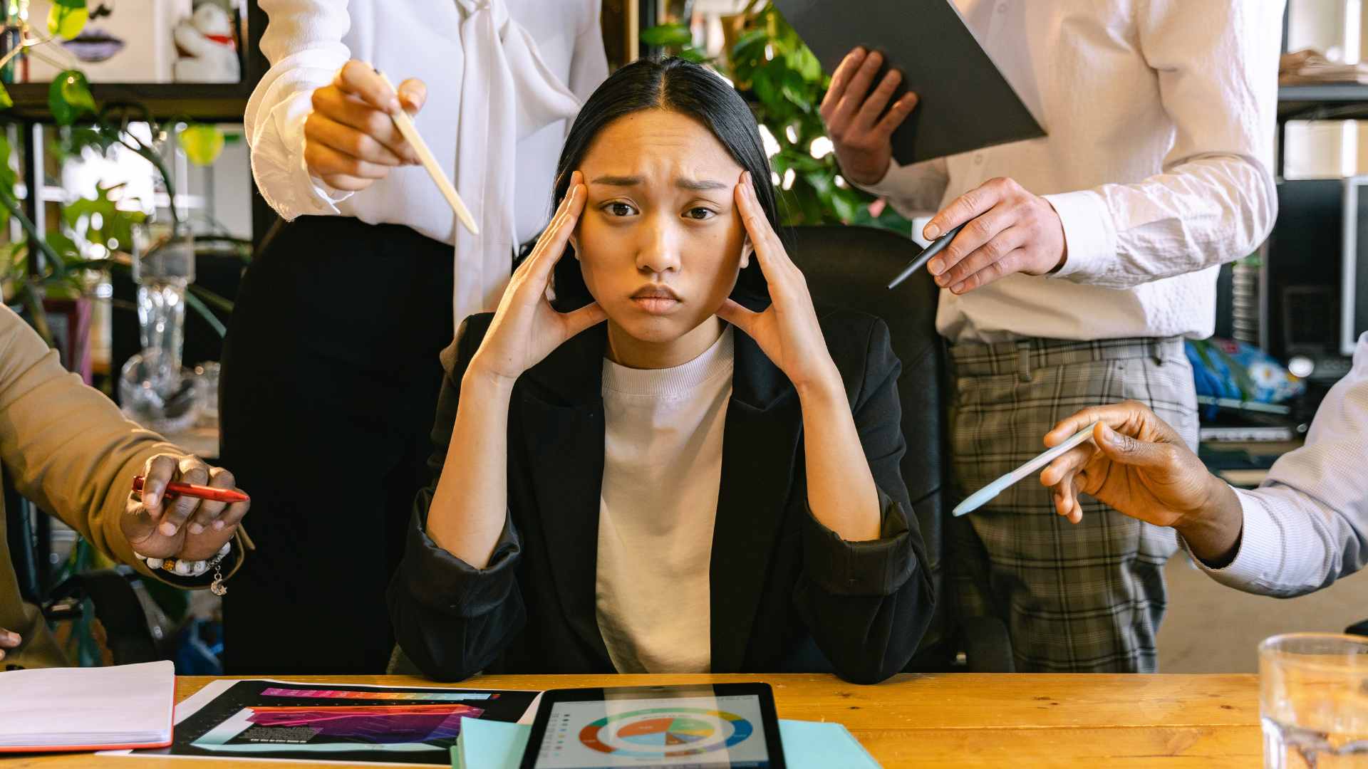 Surface Pressure | Therapy for Perfectionists in Tigard, OR | Online Anxiety Counseling in Oregon A woman sits at a desk looking stressed while multiple people around her hold out documents and devices, demanding her attention. Perfectionism can be overwhelming.