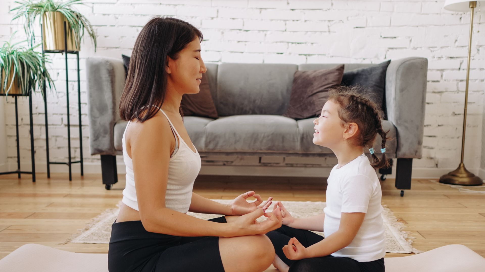 Mindfulness for Families | Tigard, OR therapy for families An adult and a child sit cross-legged on yoga mats indoors, facing each other with eyes closed and hands in meditation poses, practicing mindfulness together. Mindfulness techniques for families in Tigard, OR.