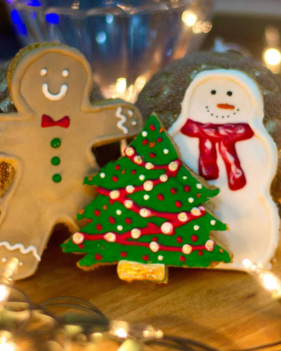 Decorated cookies | Online therapy in Oregon | Best therapist in Tigard, OR | Anxiety therapy in Oregon Three decorated cookies shaped like a gingerbread man, a Christmas tree, and a snowman are displayed on a wooden surface with blurred lights in the background. Get support for your mental health from the best therapist in Tigard, OR and online therapist in Oregon.