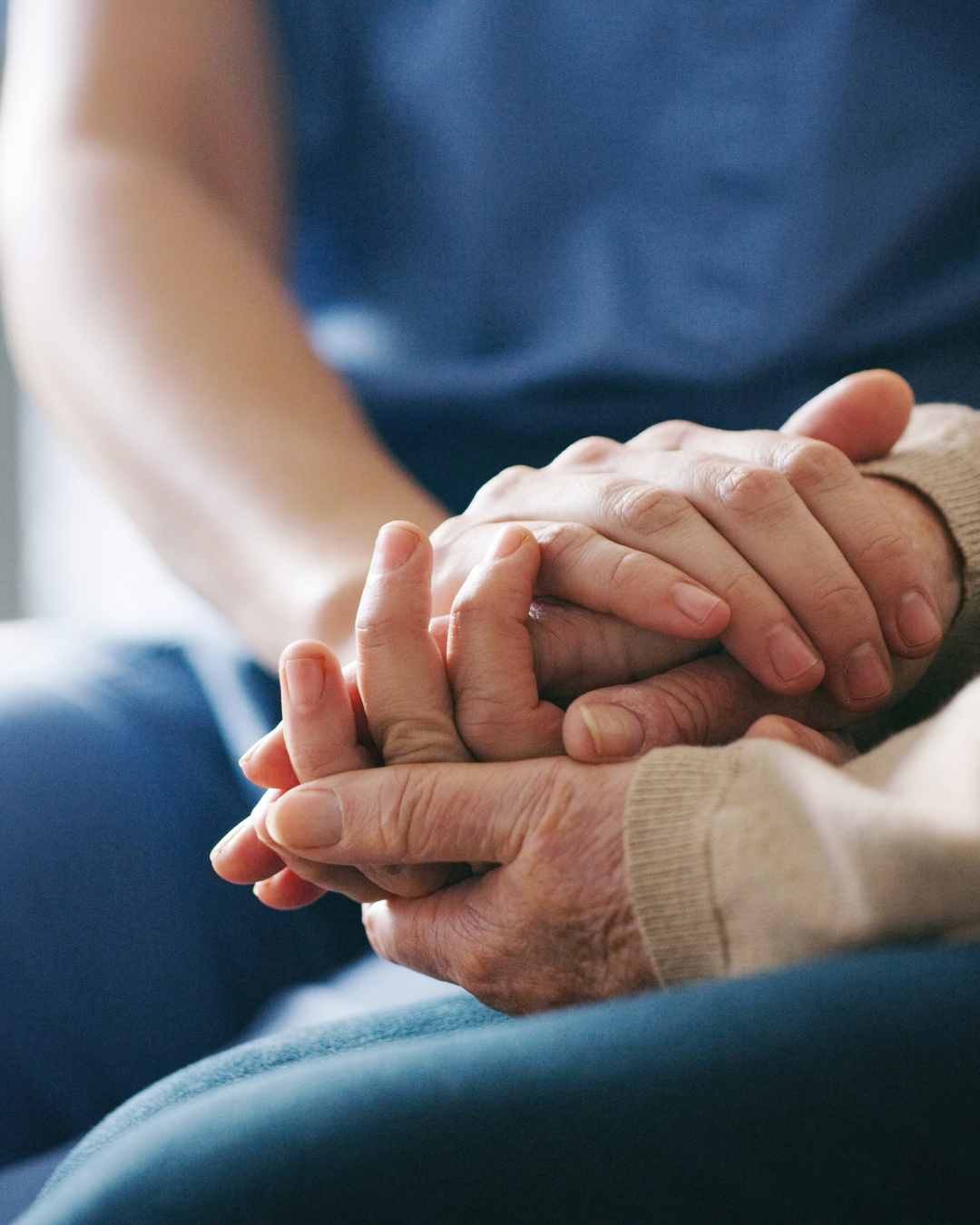 Close-up of a younger person gently holding the hands of an older person, suggesting care and support. Consider online therapy in Oregon here.