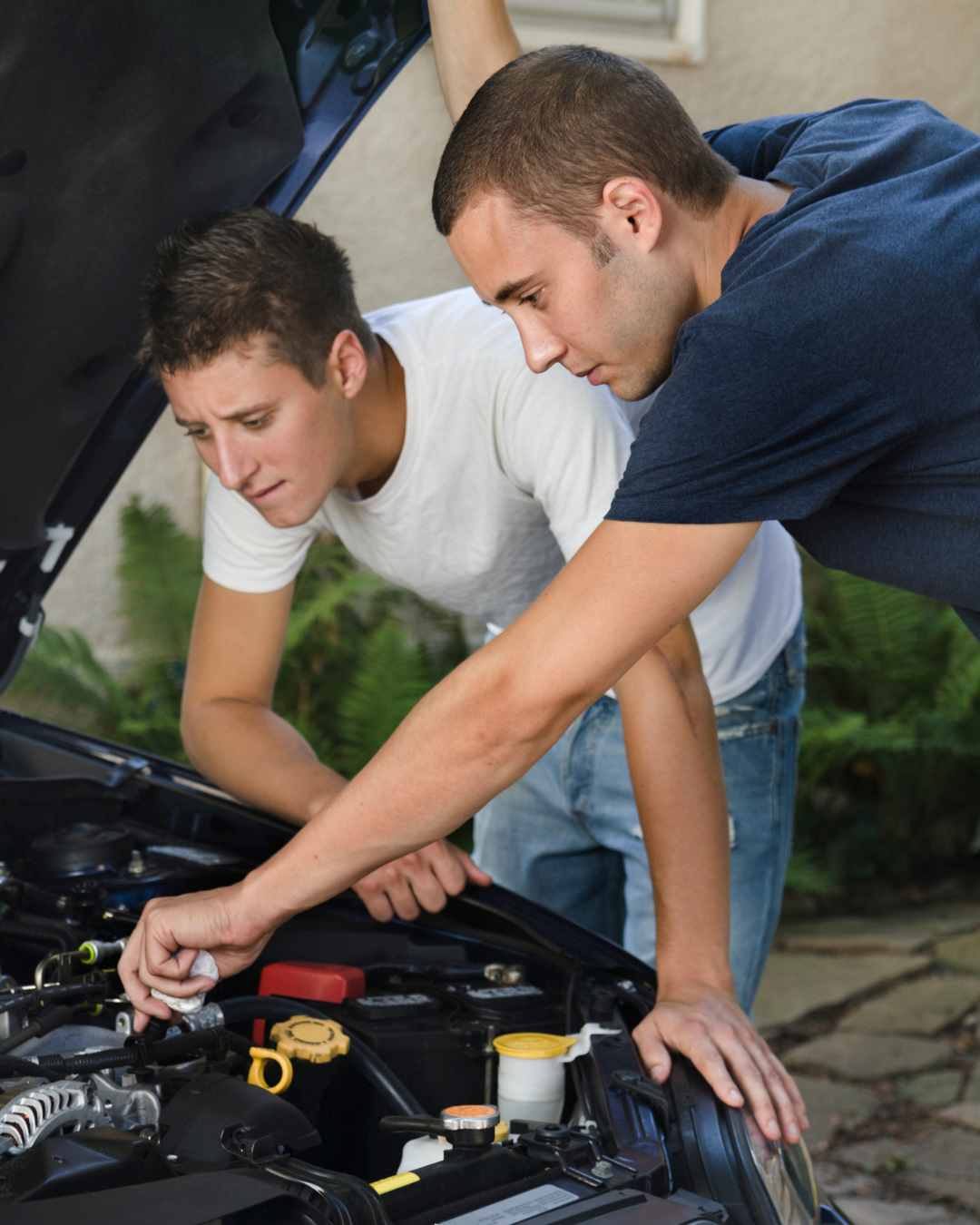 Two young men are inspecting the engine of a car with the hood open, one reaching inside while the other observes closely. Is it time for a mental health tune-up? Talk with a therapist in Tigard, OR today!