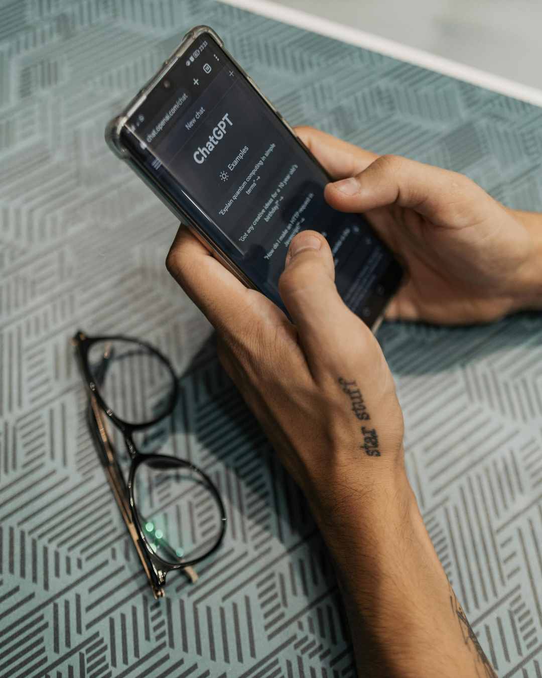 A person holding a smartphone displaying the ChatGPT webpage, with eyeglasses resting on a patterned surface nearby. Can ChatGPT be your therapist? Learn why AI cannot replace real therapy and how human connection supports healing in Tigard, OR.